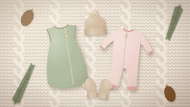 Flat lay of winter newborn essentials on a cream cable-knit blanket: knit baby hat, mittens, sage sleep sack and a striped zip footie sleeper